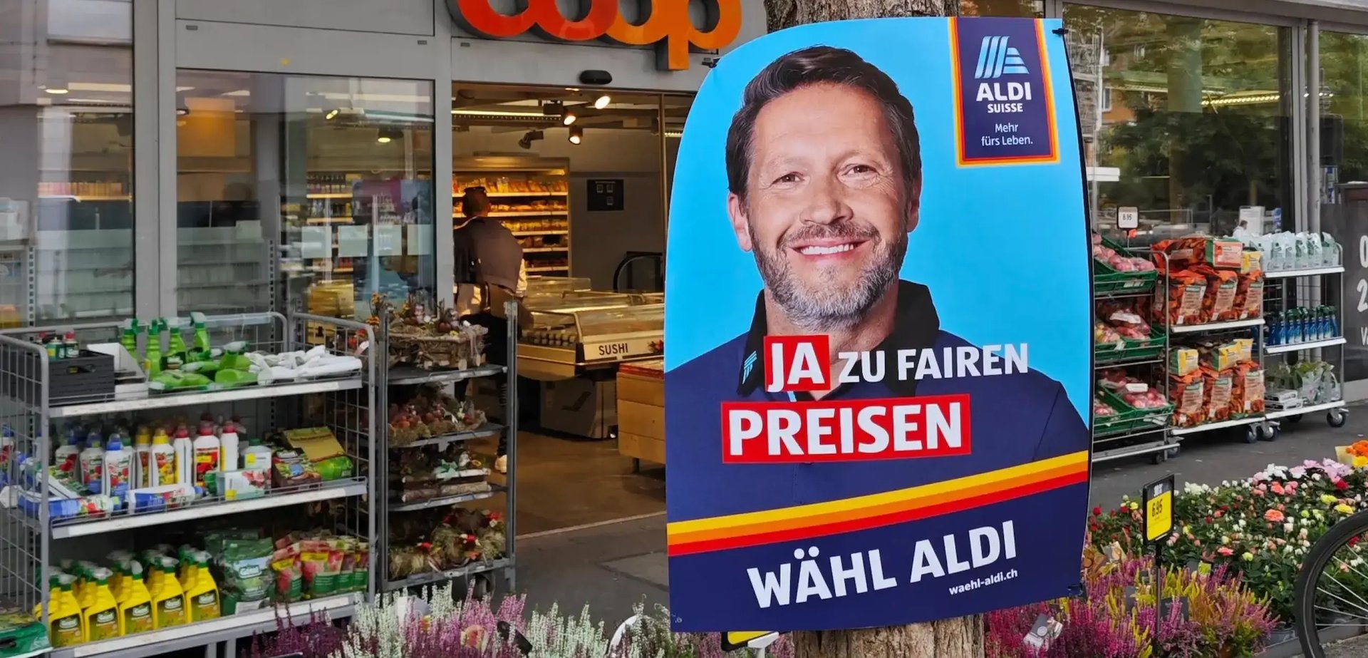 Ein Wahlplakat von ALDI SUISSE vor einer Filiale von Coop.