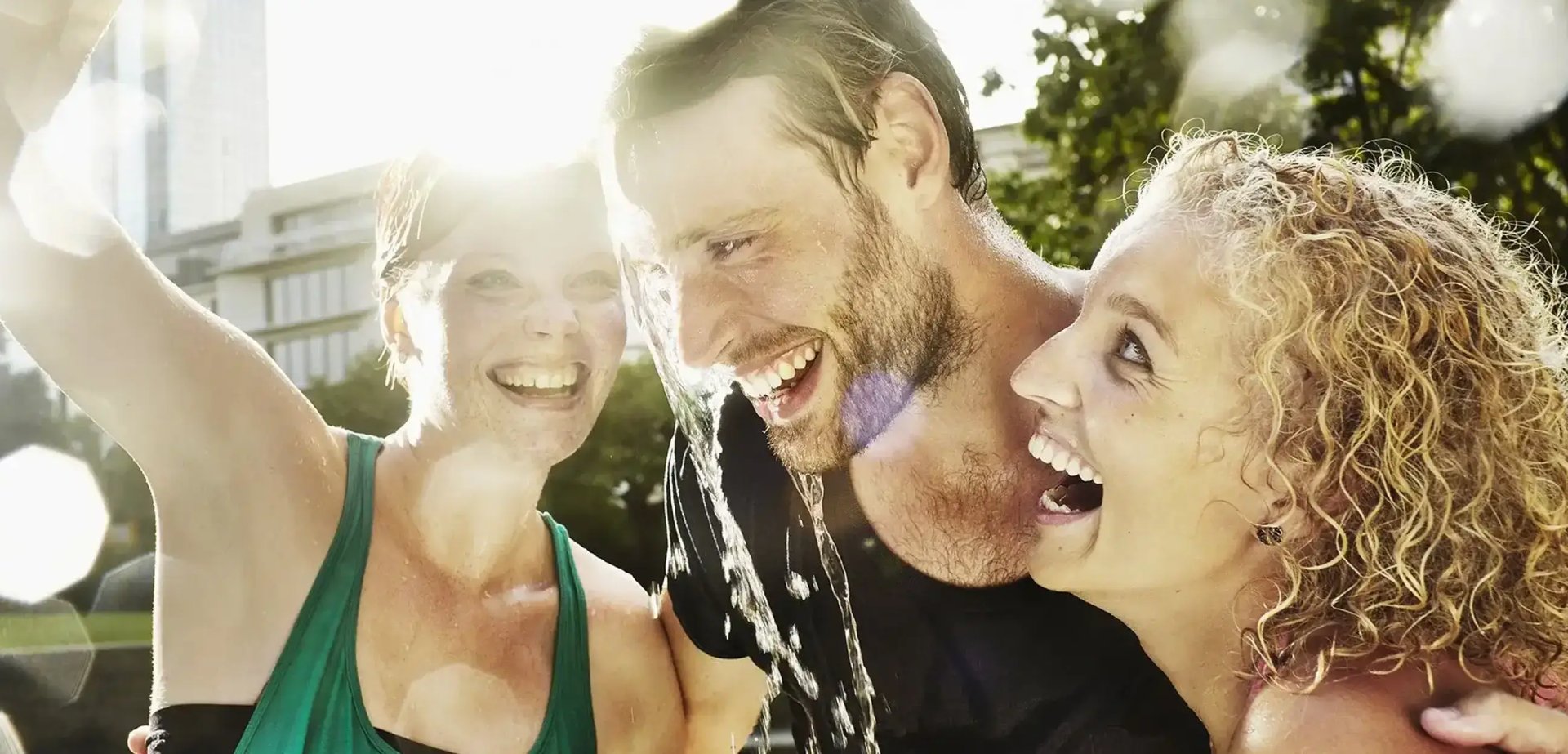 Zwei Frauen und ein Mann. Eine Frau kippt dem Mann Wasser über den Kopf. Alle lachen.