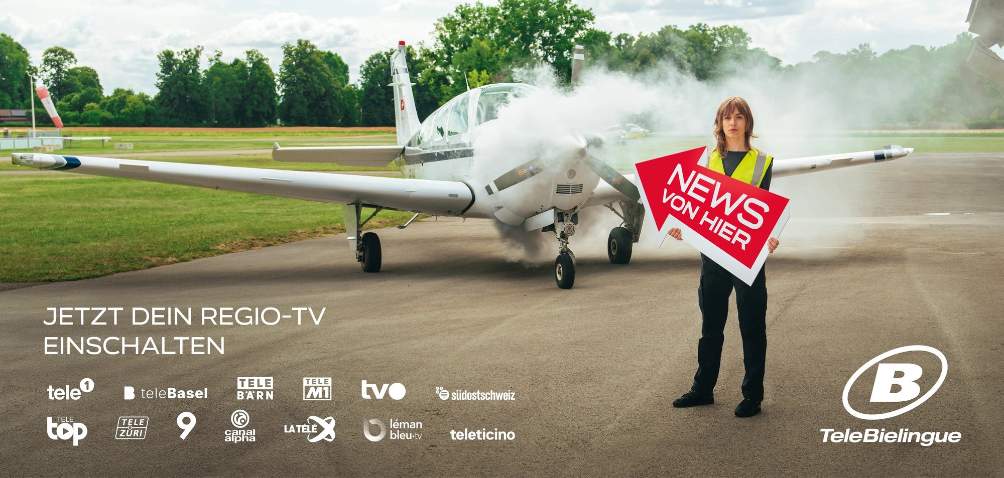 Auf einem Flugplatz steht ein Kleinflugzeug, aus welchem Rauch aufsteigt. Eine Frau steht im Vordergrund und zeigt mit einem Pfeil auf das Flugzeug. Auf dem Pfeil steht "News von hier" geschrieben.