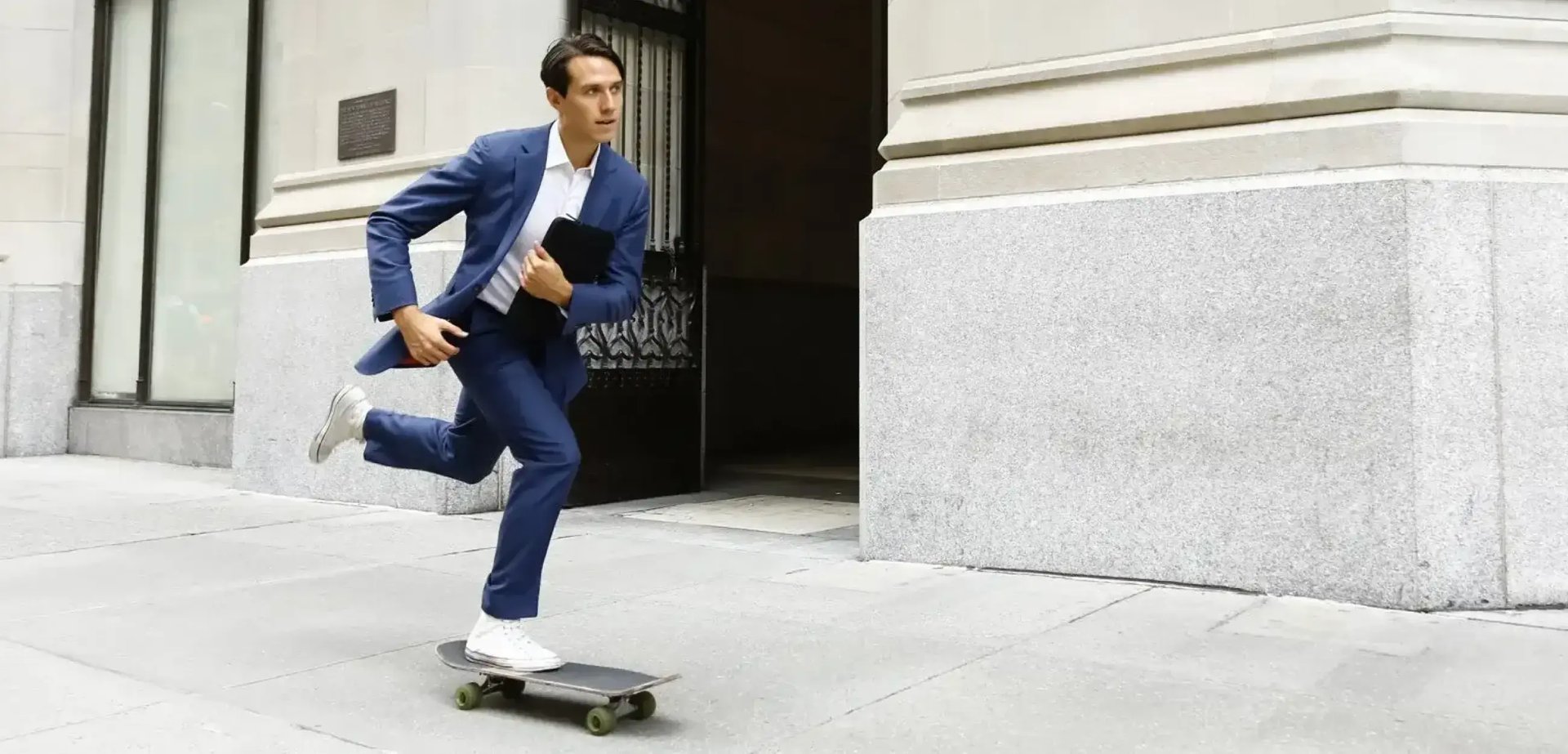 Ein Mann im Anzug fährt auf einem Skateboard auf einer Strasse.