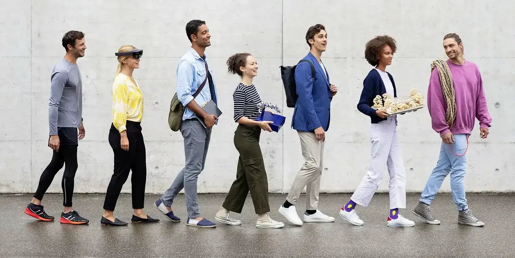 Sieben Personen laufen hintereinander einer Wand entlang.