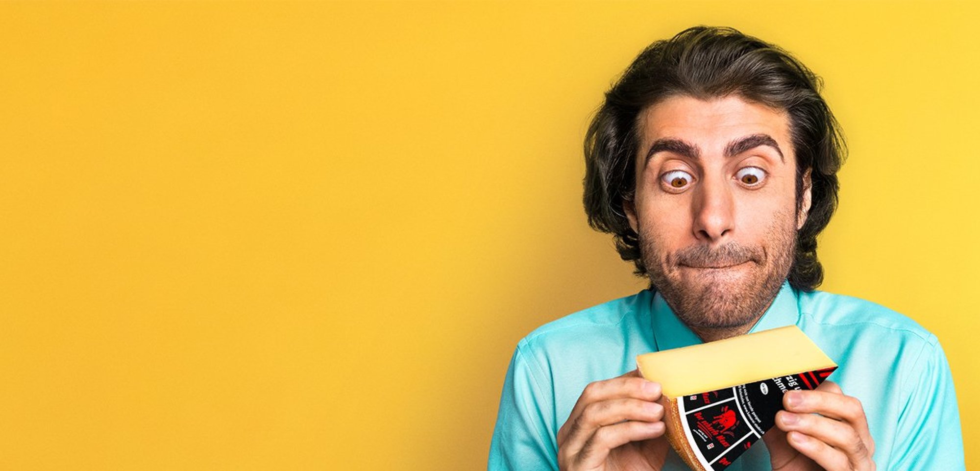 Ein Mann steht vor einem gelben Hintergrund und hält ein Stück Käse in der Hand.